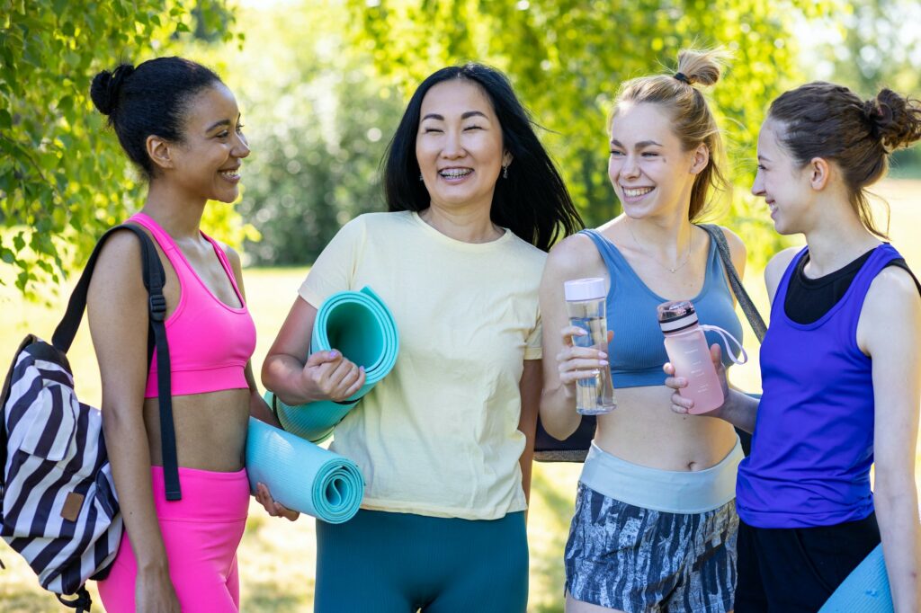 Diverse group of young beautiful girls practicing fitness outdoors in the park in summer. Concept of