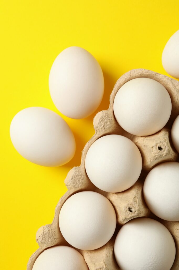 Egg box with fresh eggs on yellow background