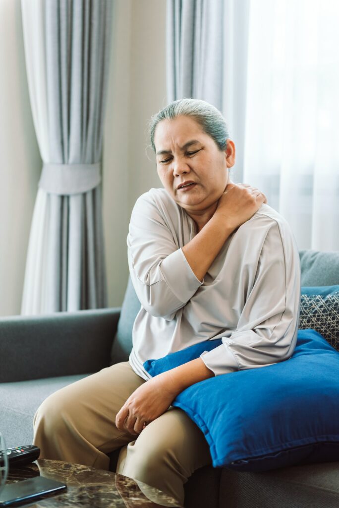 Senior asian woman has shoulder pain symptoms while sitting at living room.