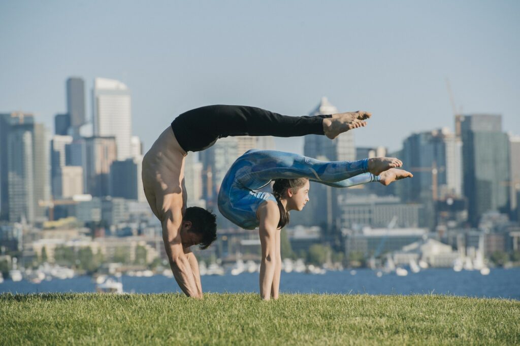Teenage girl and young man, outdoors, balancing on hands in yoga position.