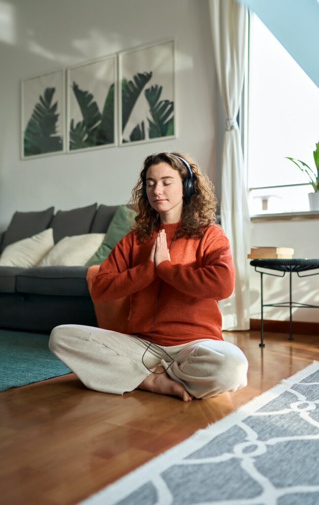 Young mindful woman wearing headphones doing meditation at home. Vertical