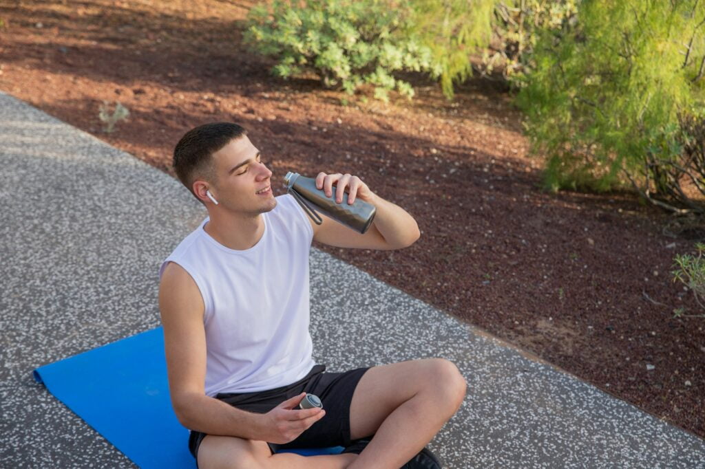 A boy drinks water while exercising outdoors, concept of hydration in sport
