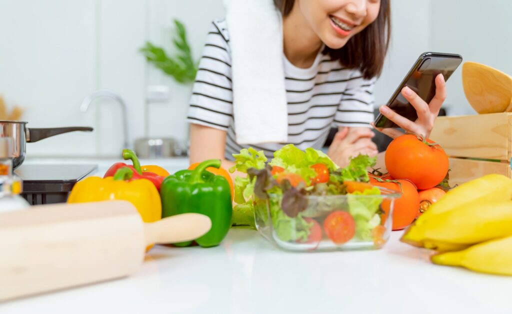 Woman hand holding a smartphone and salad bowl with tomato and various green leafy vegetables on the